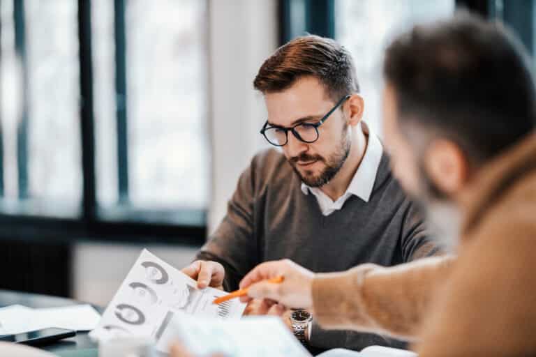 Two professional-looking men look over reports filled with data and charts.