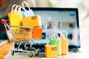 Mini shopping cart and boxes sit in front of a laptop to symbolize online sales.